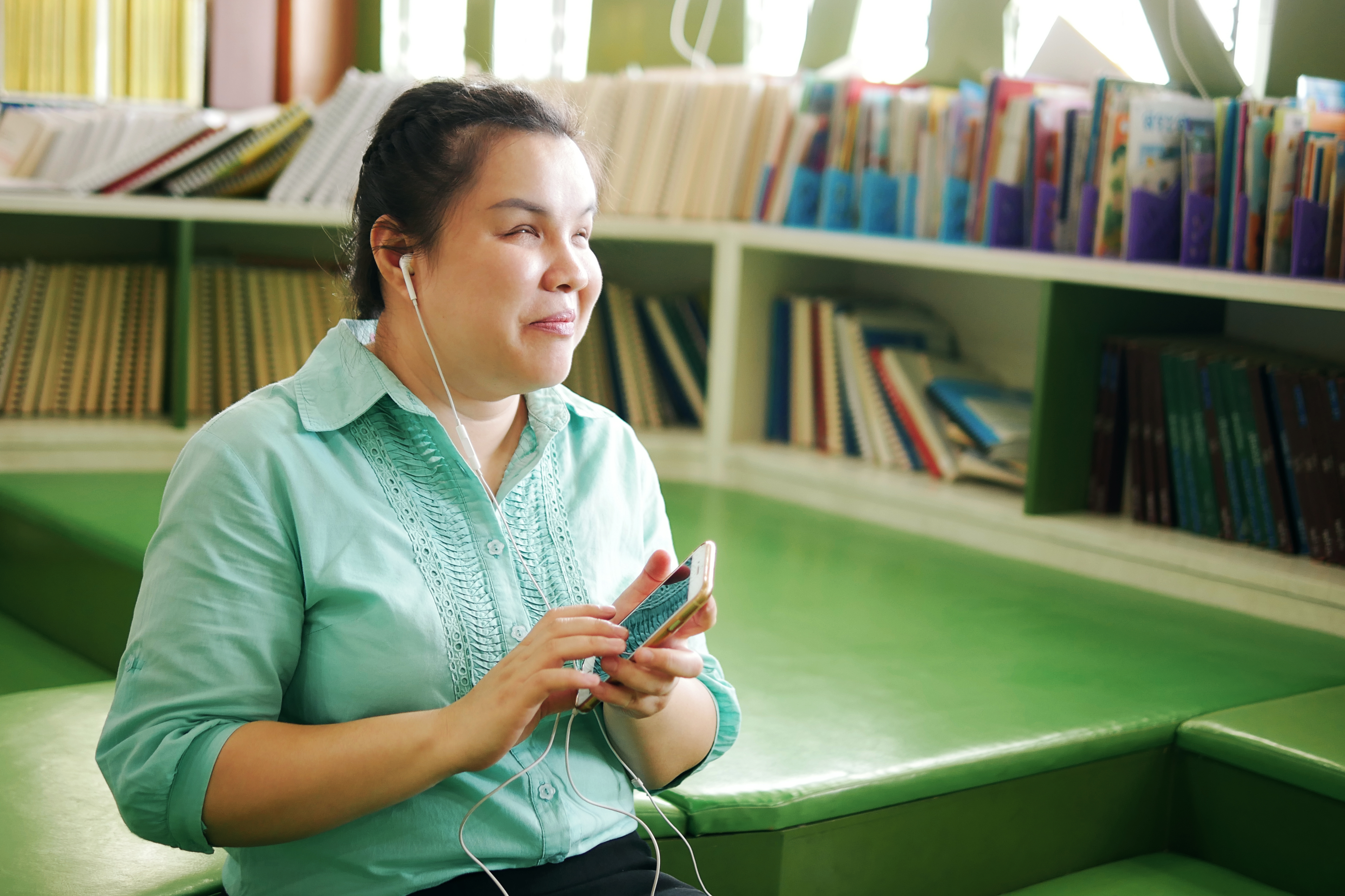 A student using Enabelo Apps independently on a mobile phone with earphones in a library setting